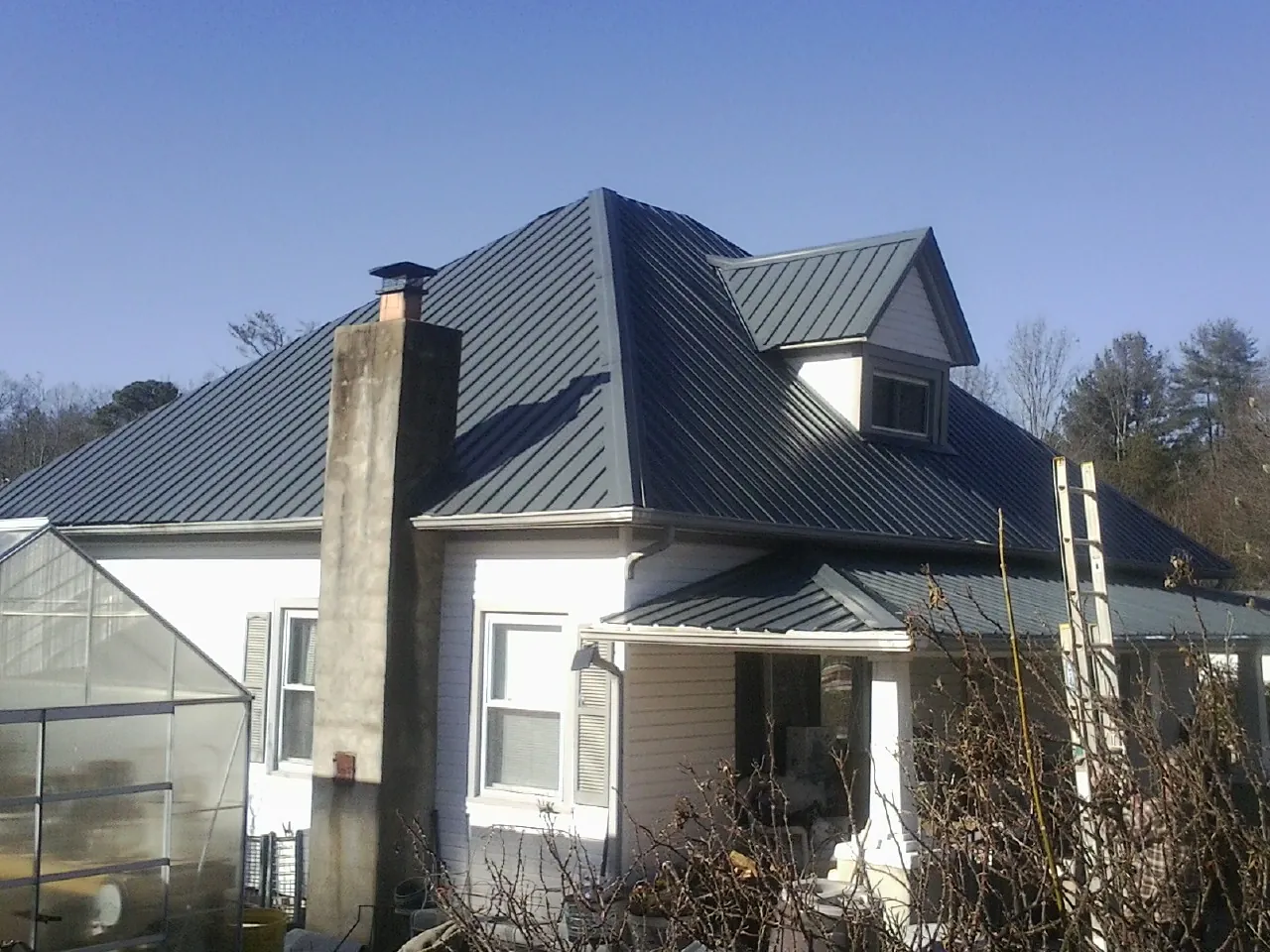 Dark blue standing seam metal roof on a white farmhouse with dormer — Slate & Tile Roof Repair by Roofing Brothers in Granger