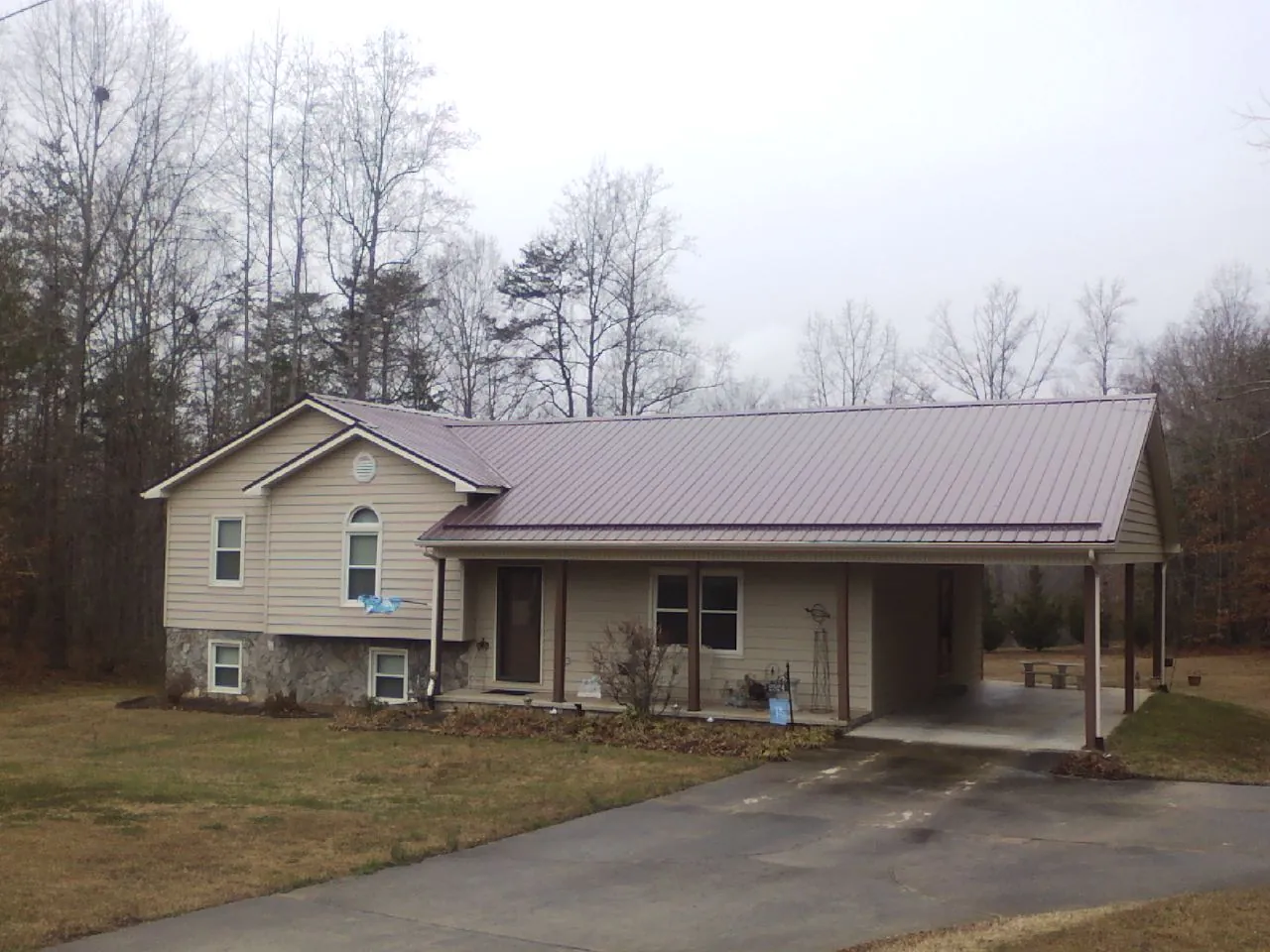 Burgundy metal roof on a tan split level home with an attached carport in Granger